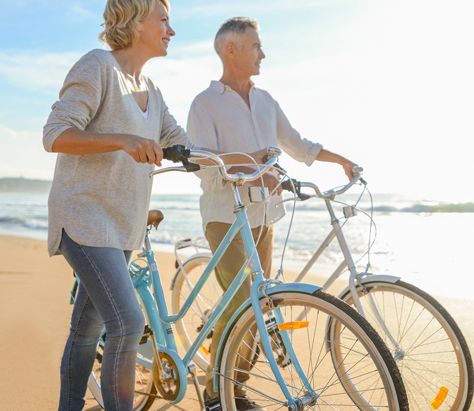 Couple nearing retirement, walking along the beach with their bikes