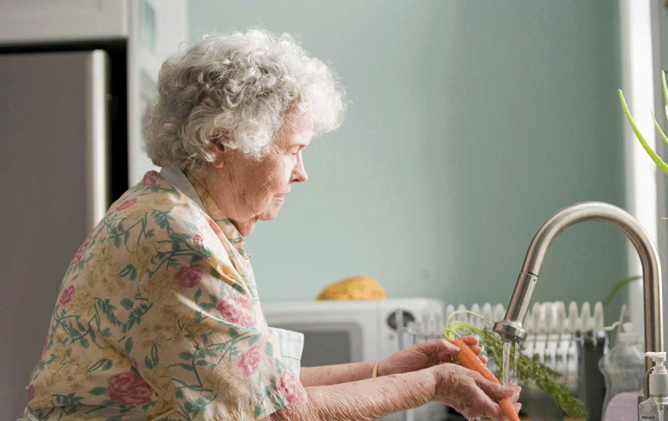 Elderly woman washing vegetables in the kitchen