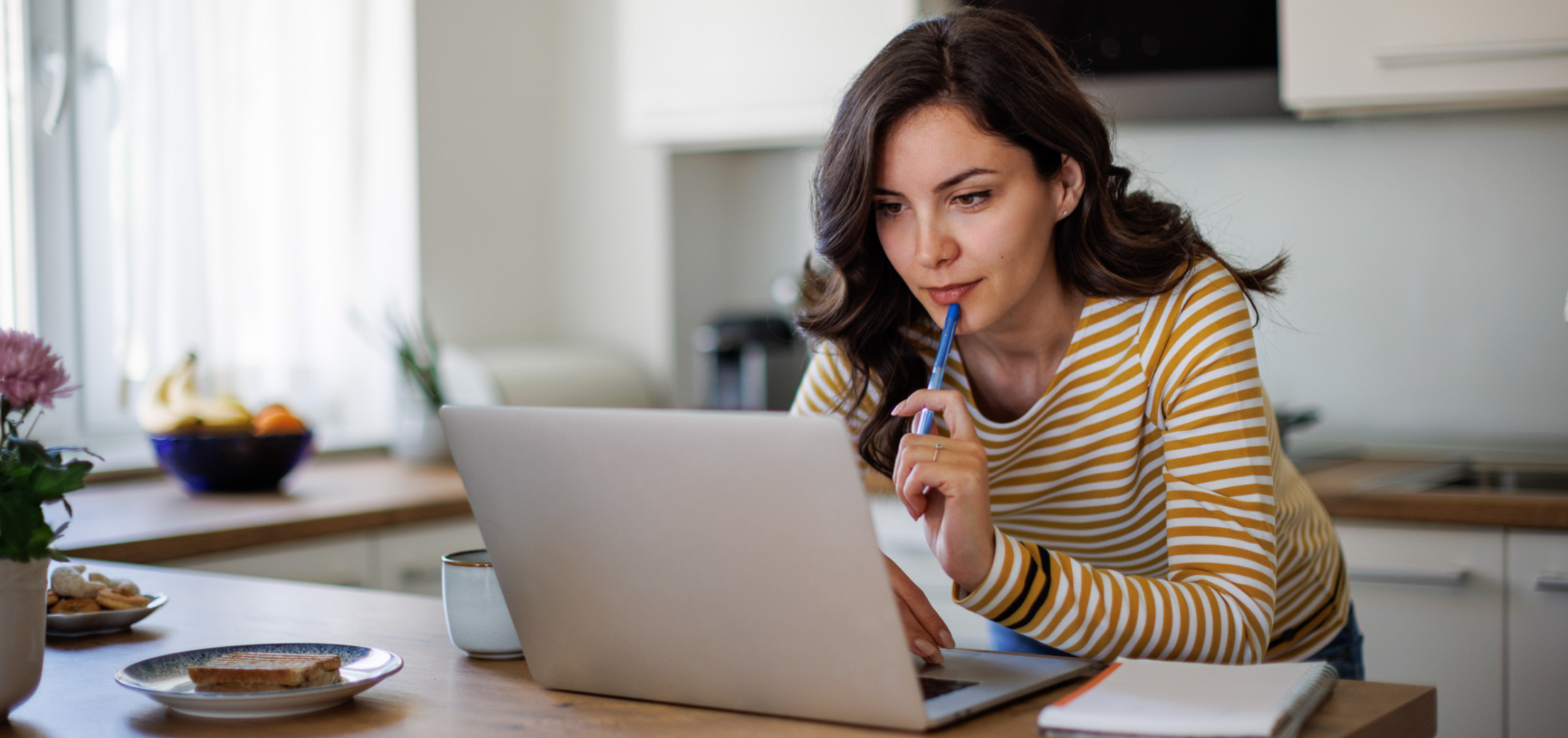 Woman looking at laptop holding a pen