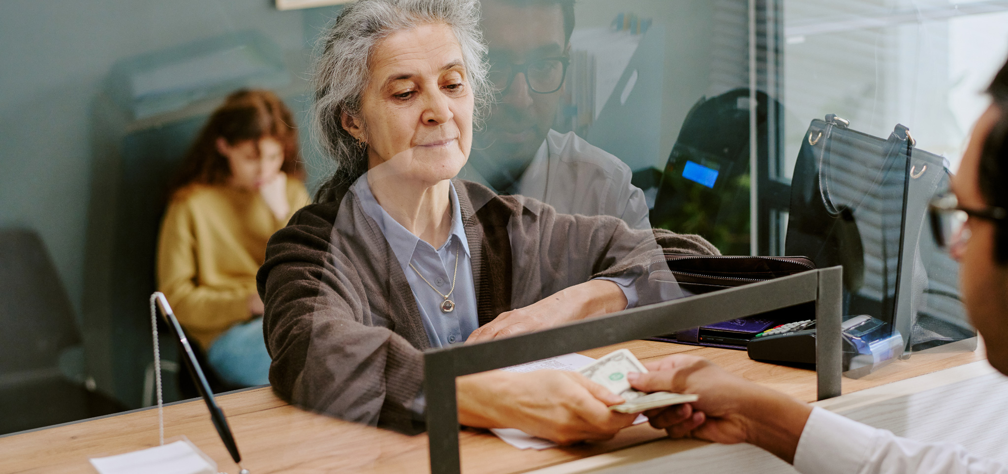 A senior woman at a teller line receiving cash
